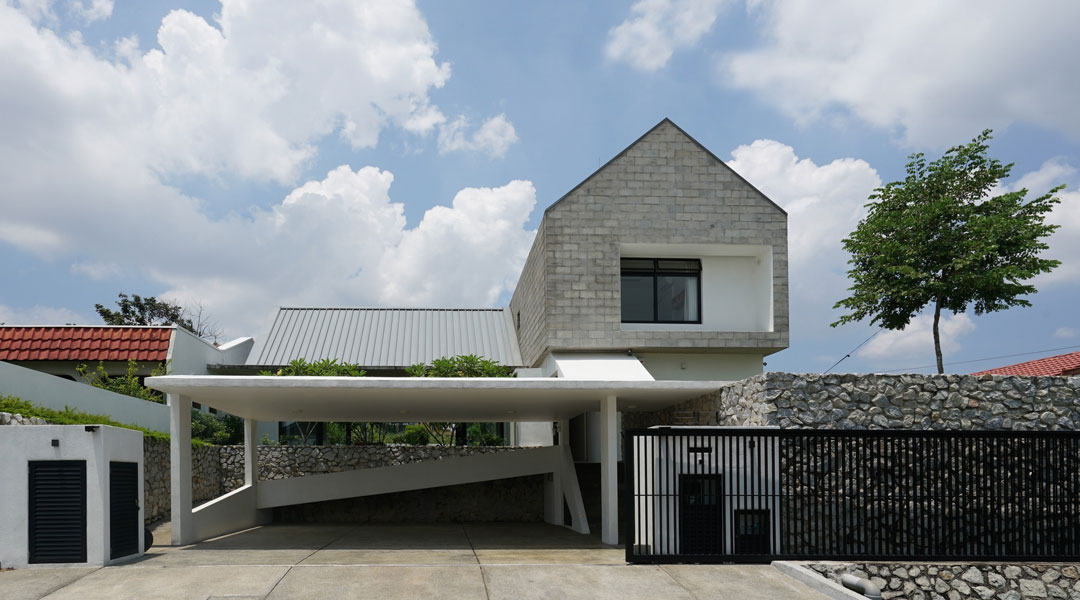 a modern two storey house design with open carport, pitched roofs, and concrete brick cladding.