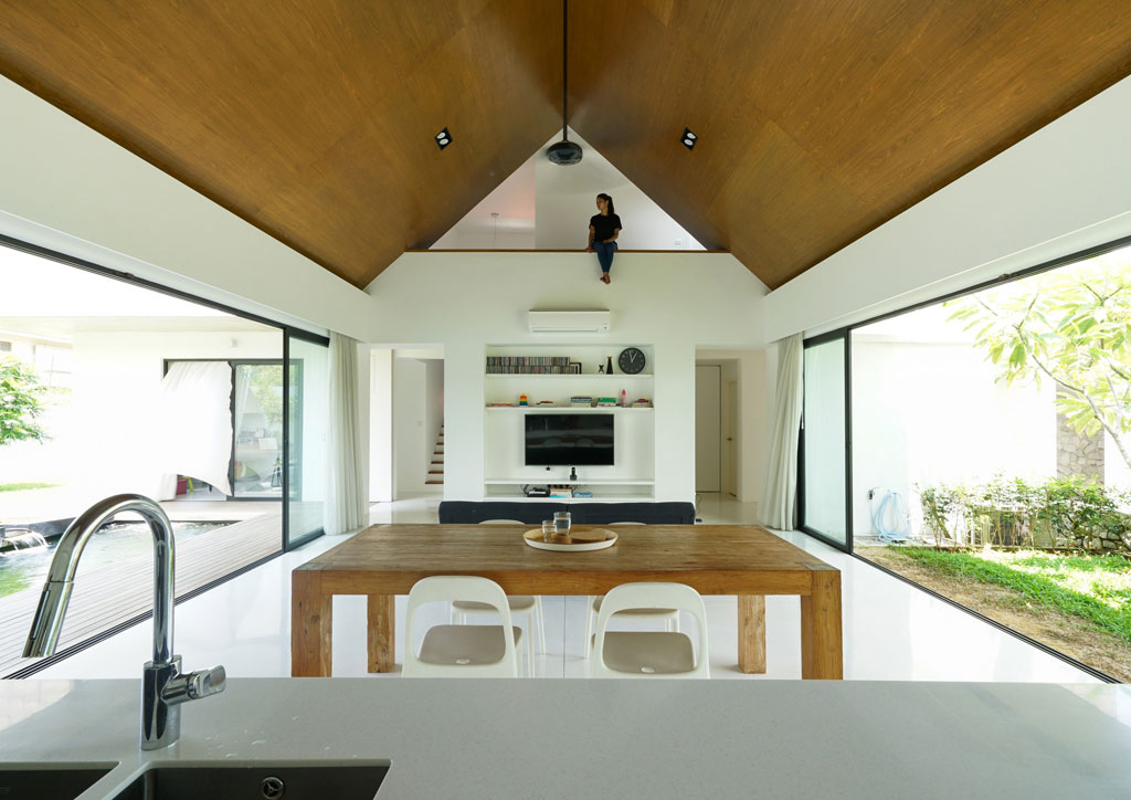 the inside of a modern two storey house design with inverted wooden ceilings above a kitchen and dining area.