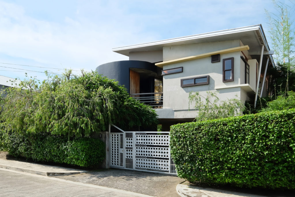 Modern bahay kubo home with a metal gate and tall hedges.