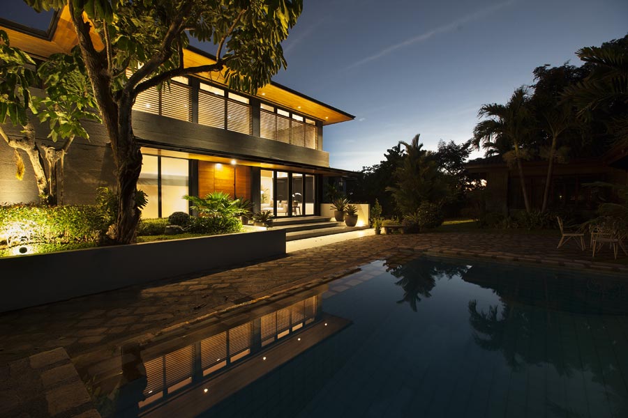 A modern two storey house design made of concrete and wooden accents overlooks an outdoor pool area.