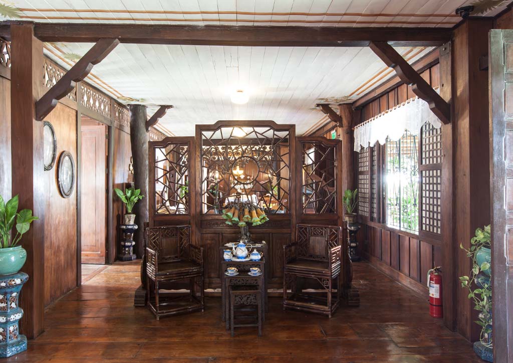 Traditional Filipino living space with ornate antique wooden chairs, hard wood floors, and capiz windows.
