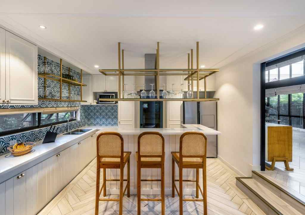 View of the kitchen with patterned tile backsplash, bar stools by the kitchen island, and brass accents
