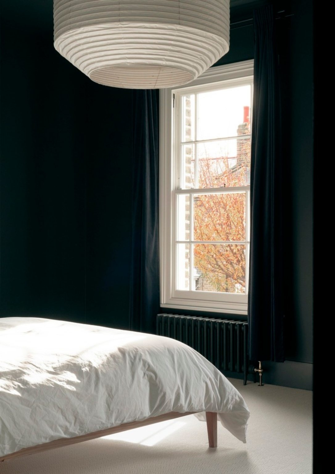 interior of modern minimalist bedroom with bed, dark walls, and paper lighting fixture