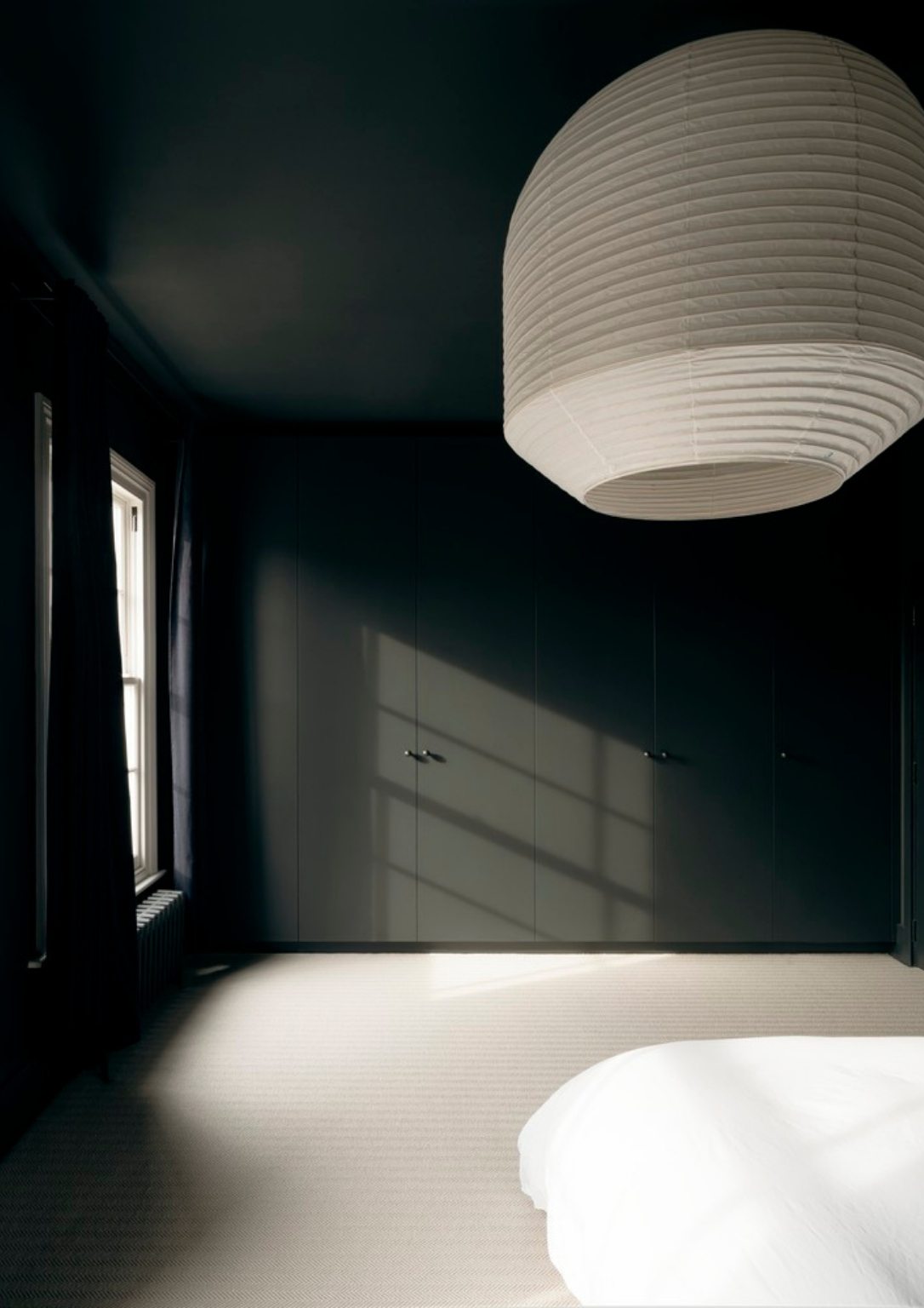 interior of modern minimalist bedroom with bed, dark walls, and paper lighting fixture