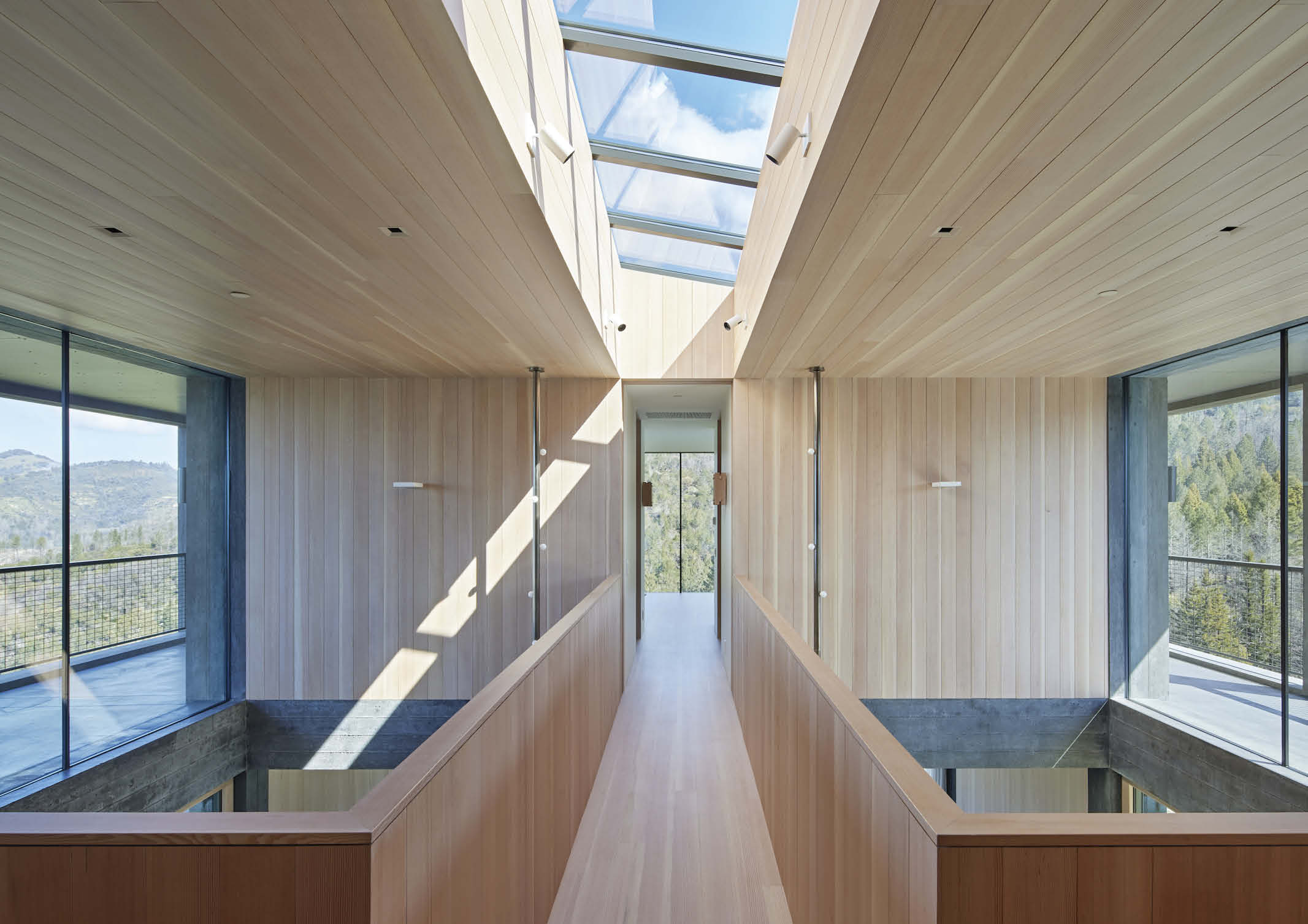 the inside of a modern two storey house design with wooden cladding on the walls and ceilings, and a skylight above a bridgeway.