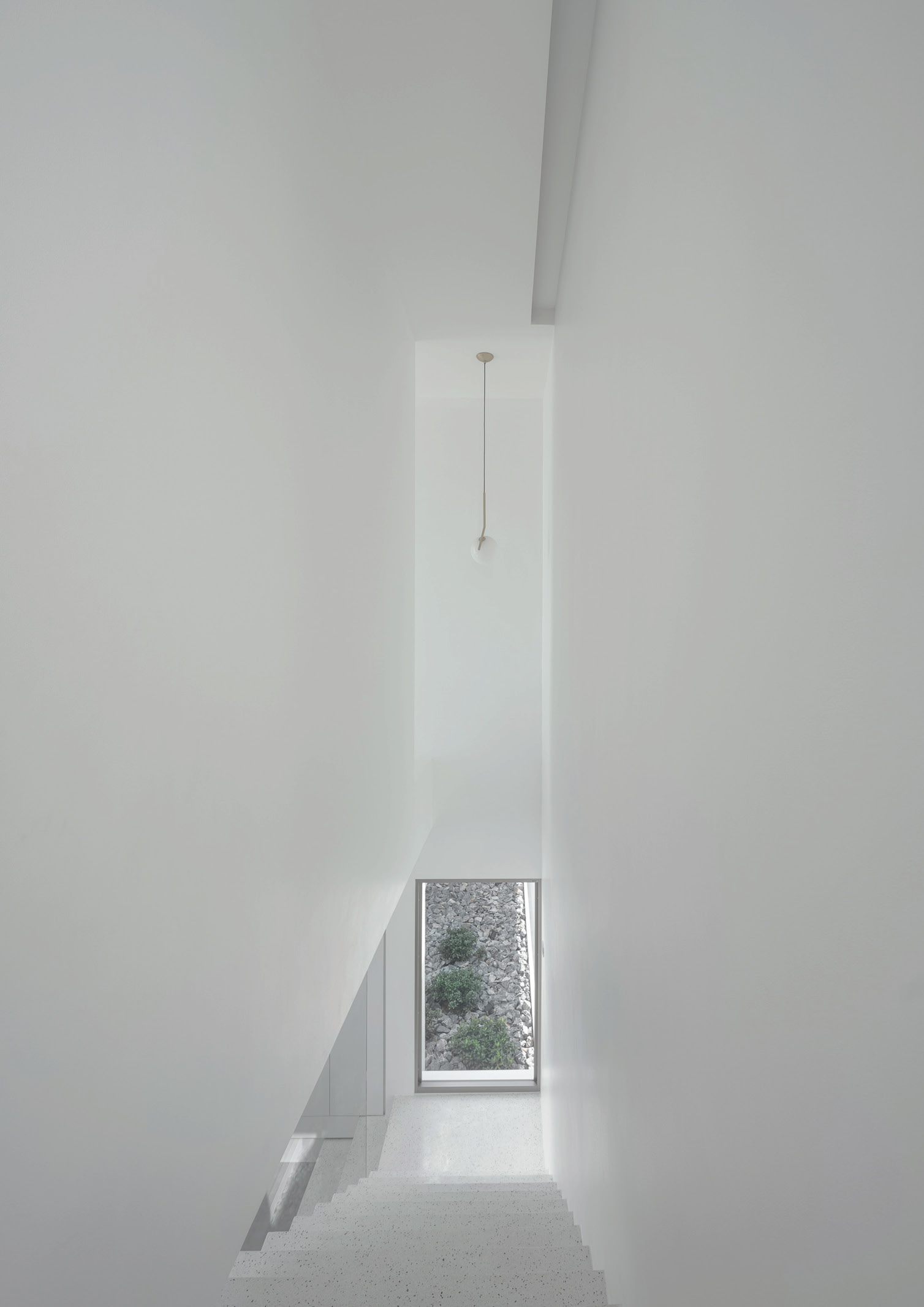 An all white stair well with a narrow window at the end.