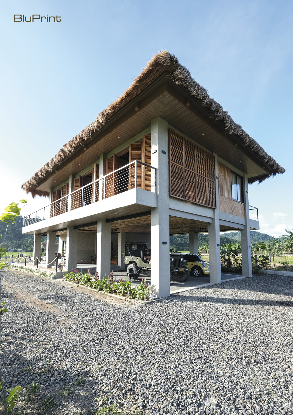 A street level view of a modern bahay kubo with concrete stilts and thatched roof.