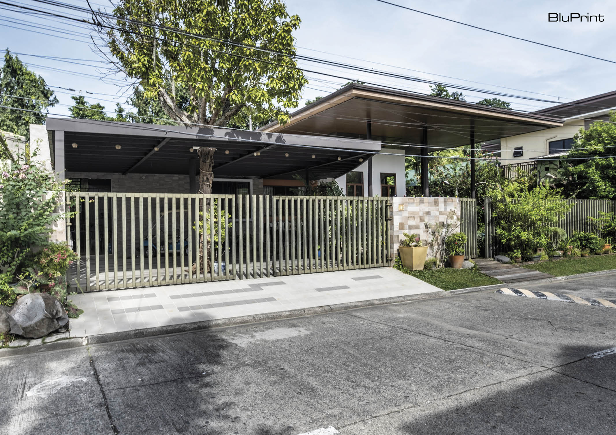 Frontage of modern home with view of the metal gate and fence, and a tree integrated into the driveway and carport