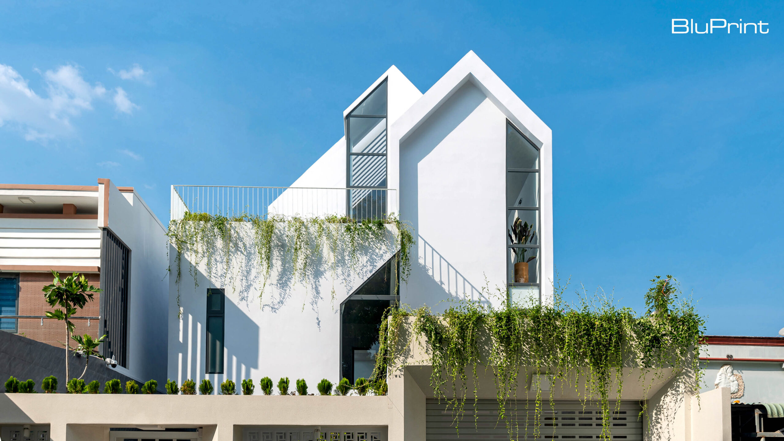 3 storey modernist white home with pitched roofs, vines hanging above the car port.