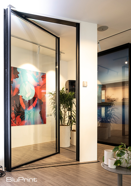 a floor to ceiling pivot door with artwork and potted plants in the background