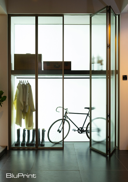 Sleek storage area with a bicycle, rain coats, and rain boots behind modern glass doors