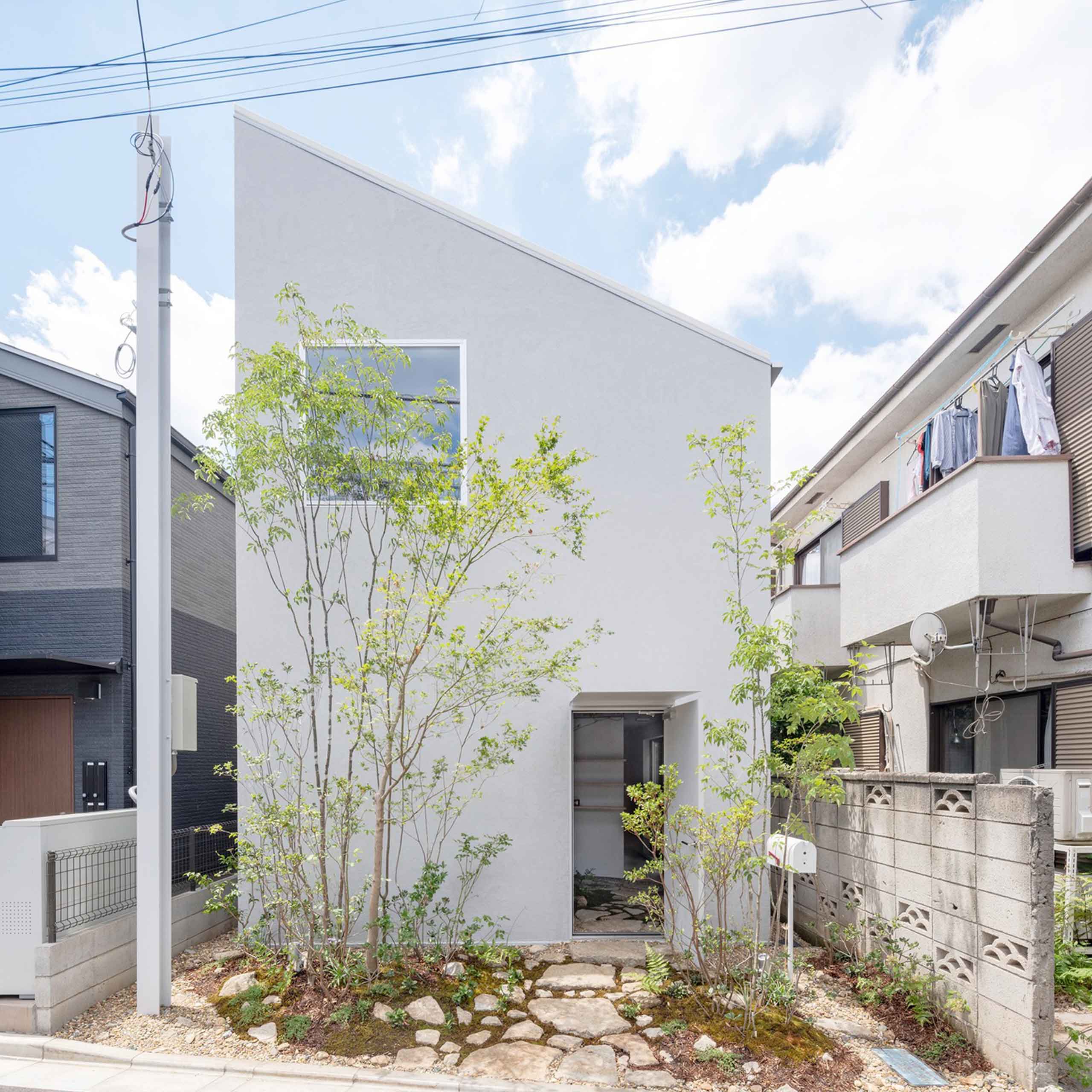 A small modern Japanese home with a white walls and pitched roof on a narrow lot.