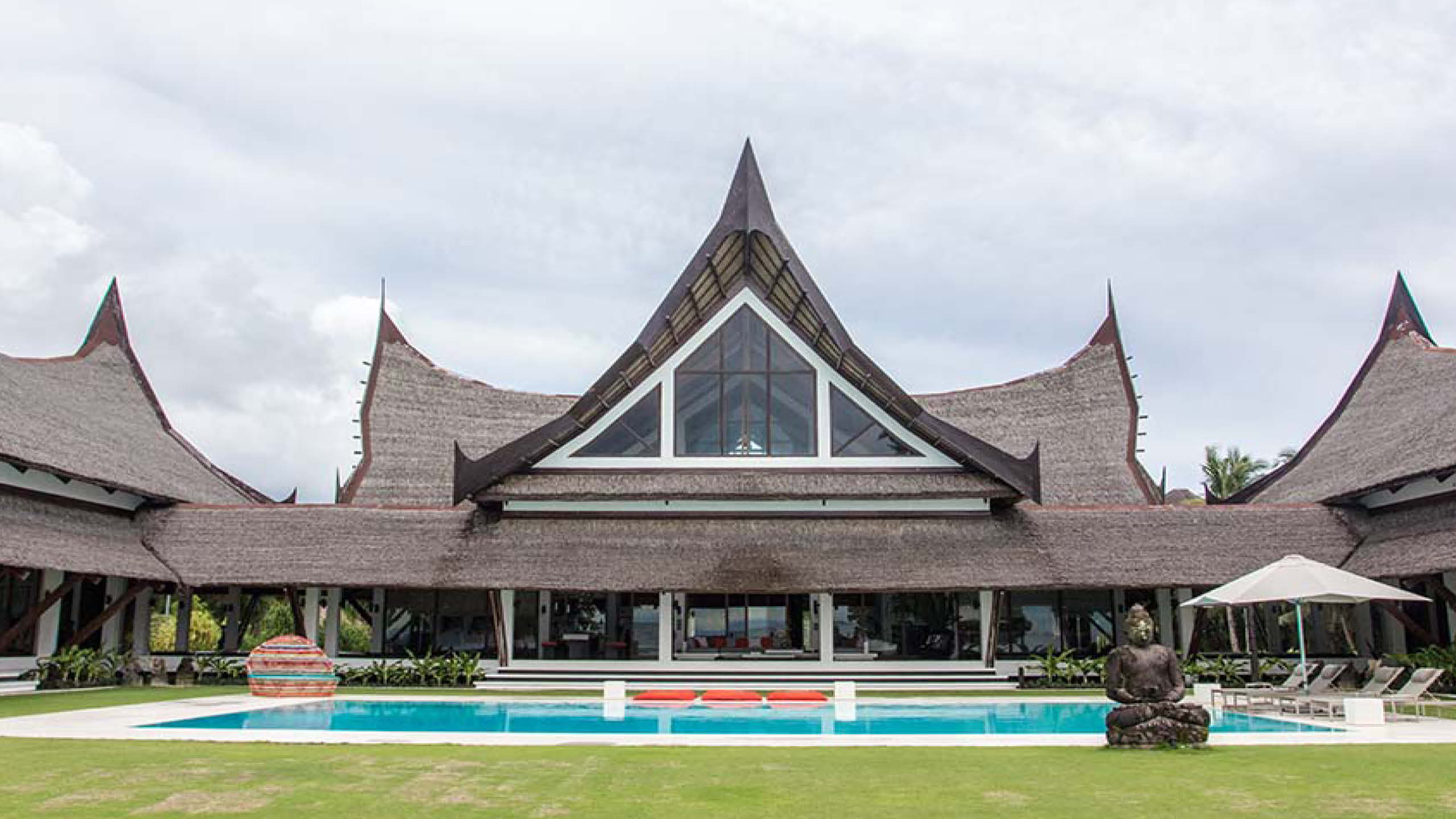 A large resort featuring nipa hut design with tall thatched roofs and a pool.