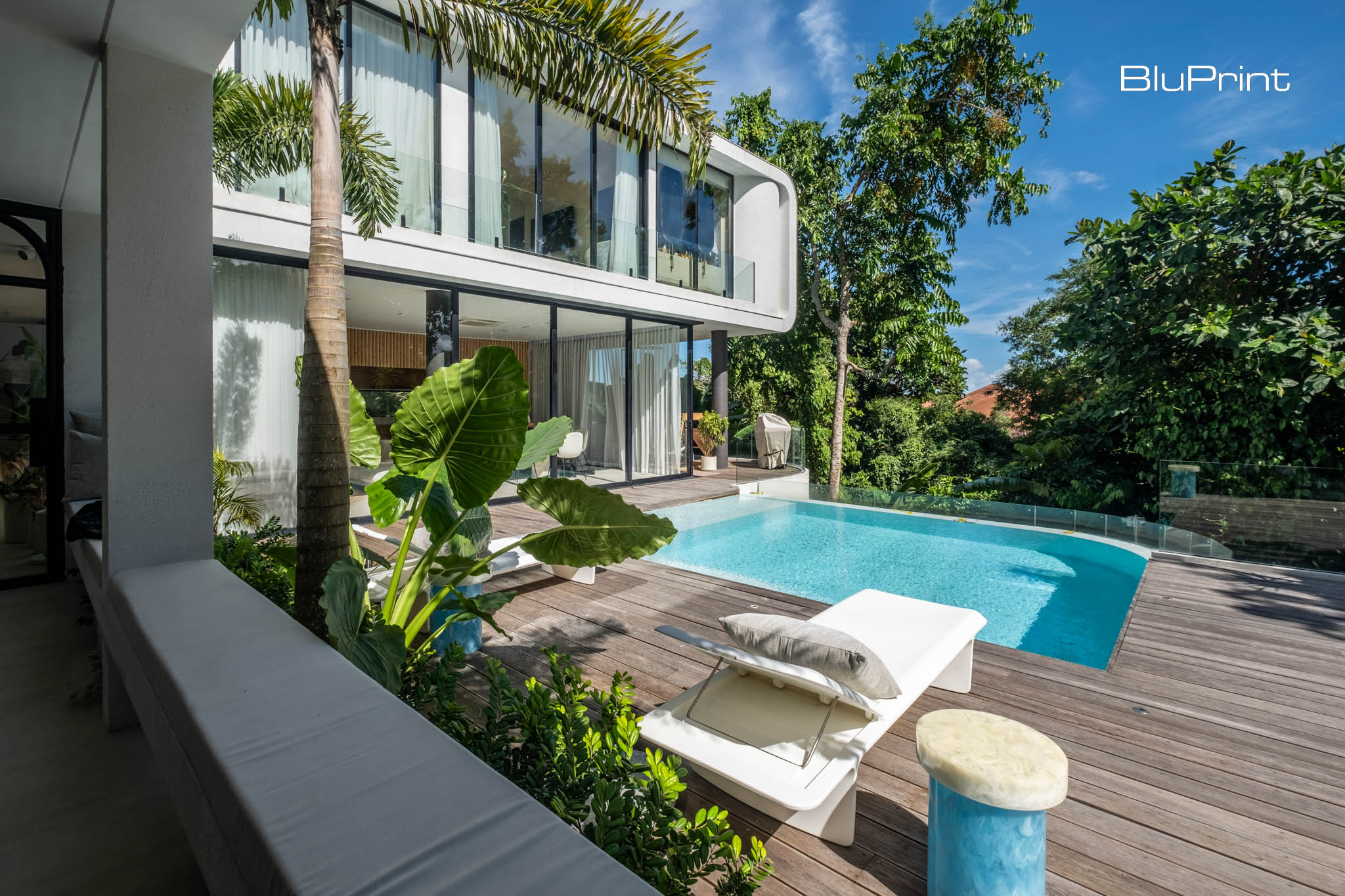 A modern tropical home with floor to ceiling windows looking out into a pool with wooden deck.