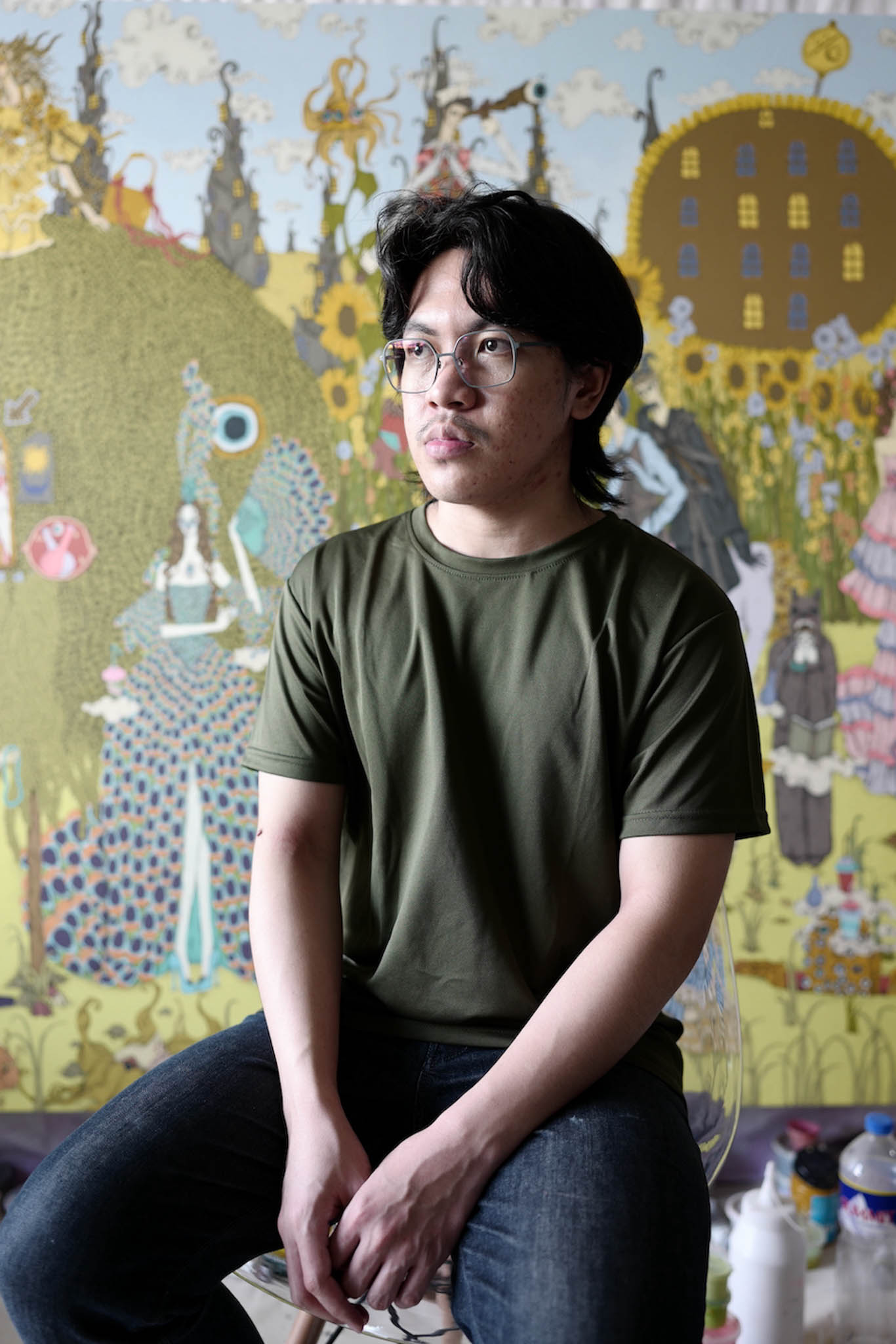 A male visual artist sitting in front of his work.