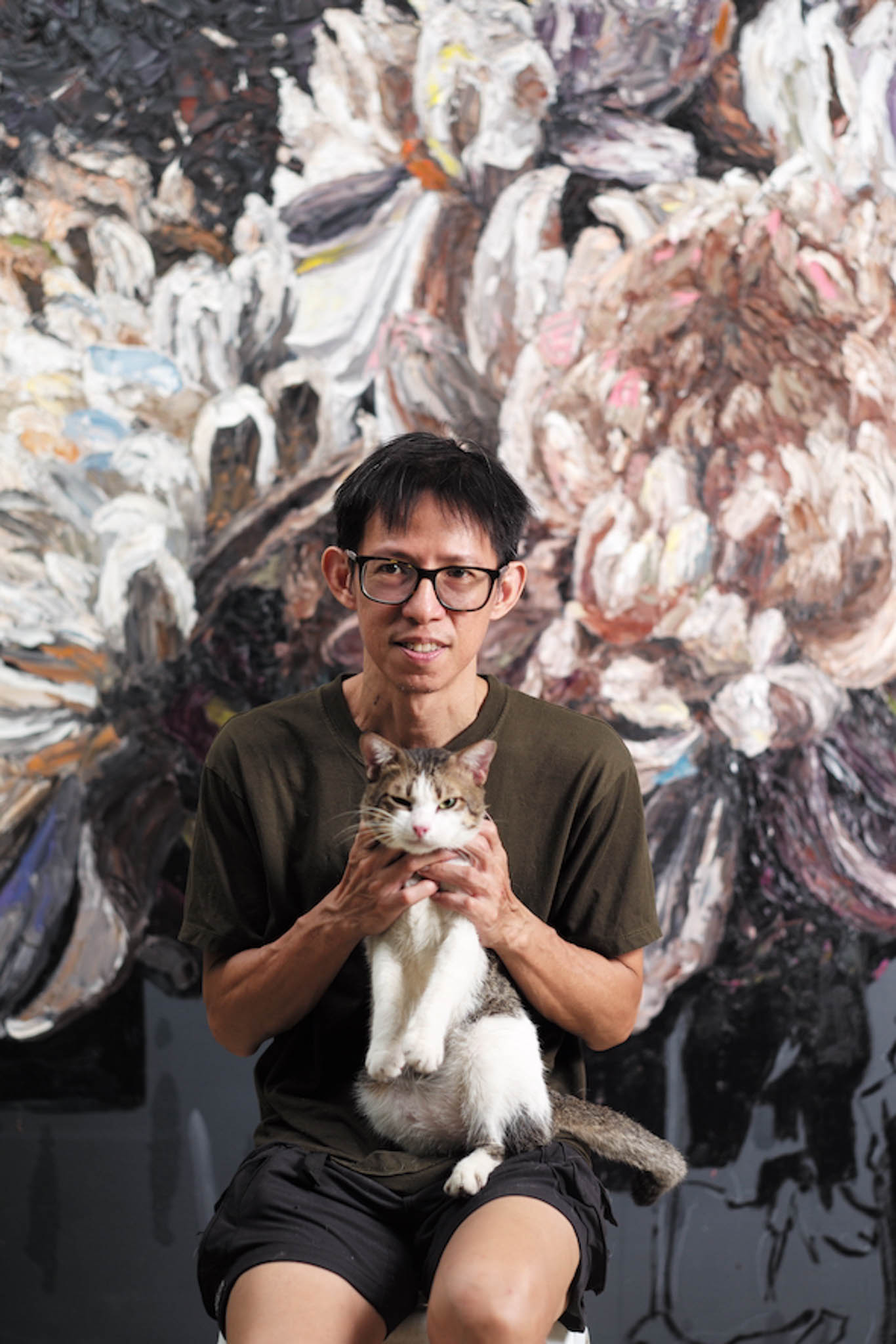 An artist holding his pet car while sitting in front of his abstract art work.