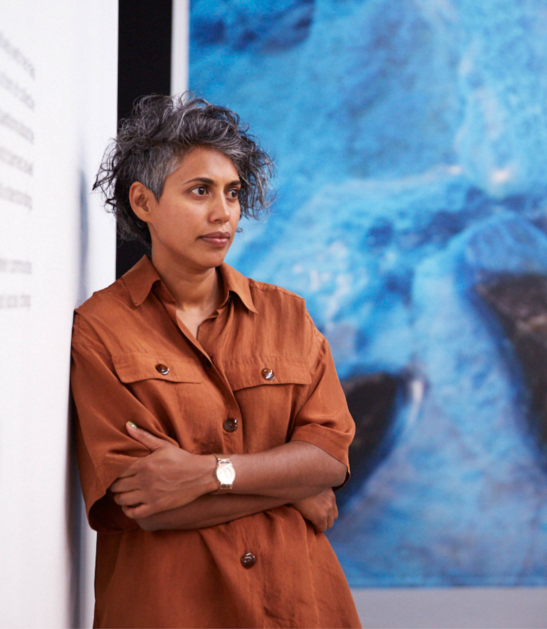 An artist stands against the wall with a large blue piece of art in the background.