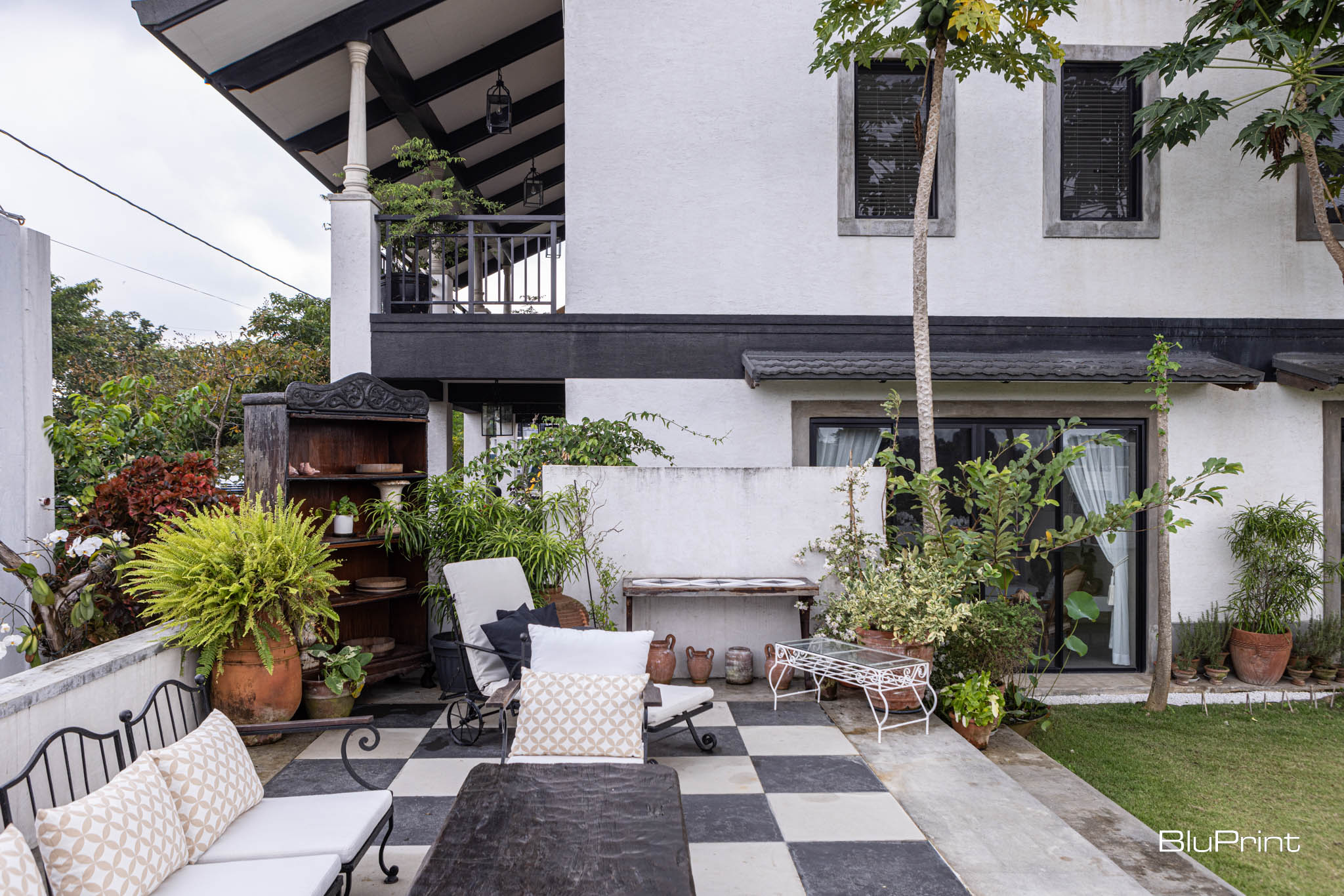 An open and airy veranda area with metal framed seating next to a 2-storey home.