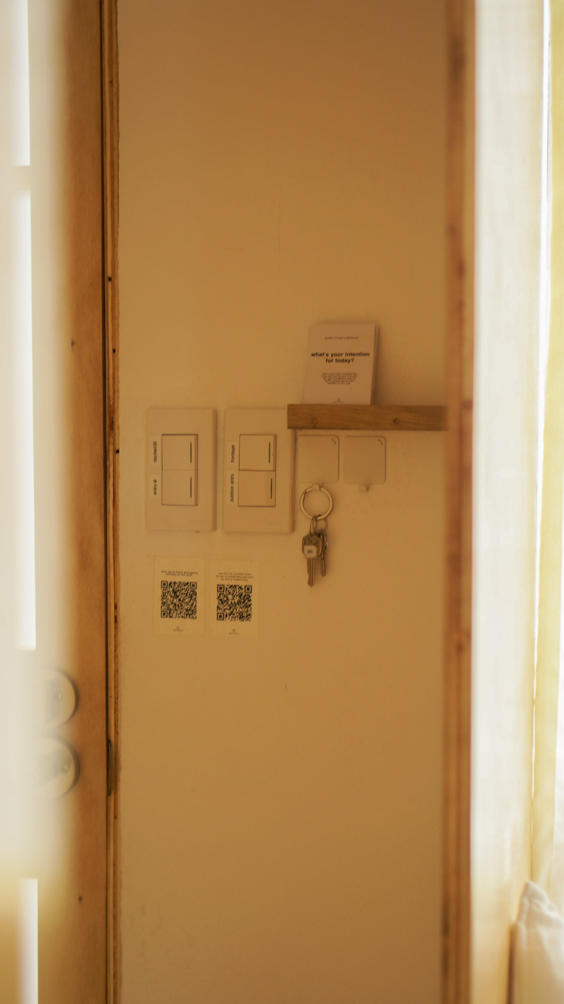 A small nook in an entryway with light sockets, hooks for keys, a small shelf, and QR codes inside a  small house design.