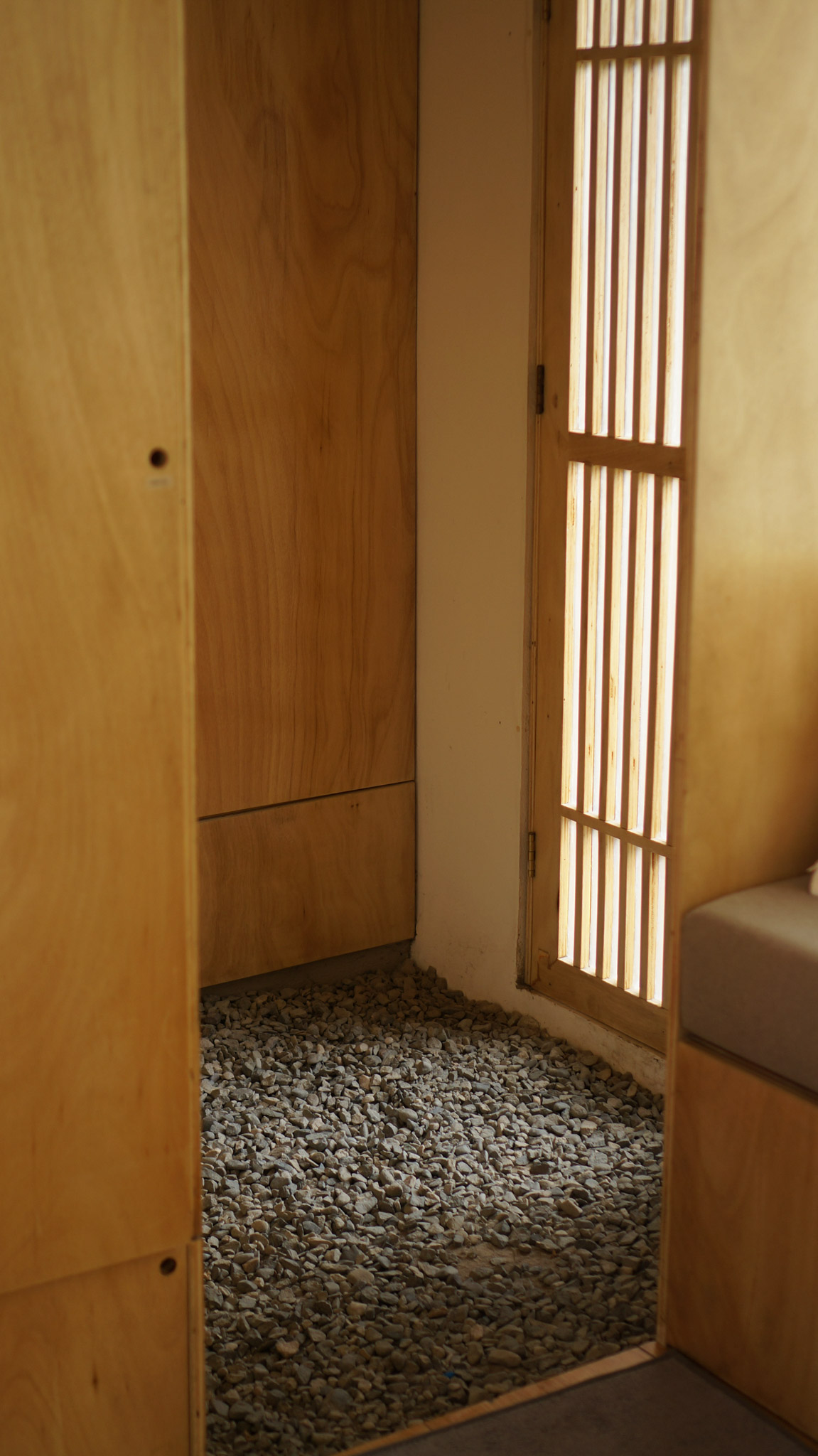 A small house design's little foyer with gravel on the ground and the detail of the front door inspired by Japanese shoji screens.