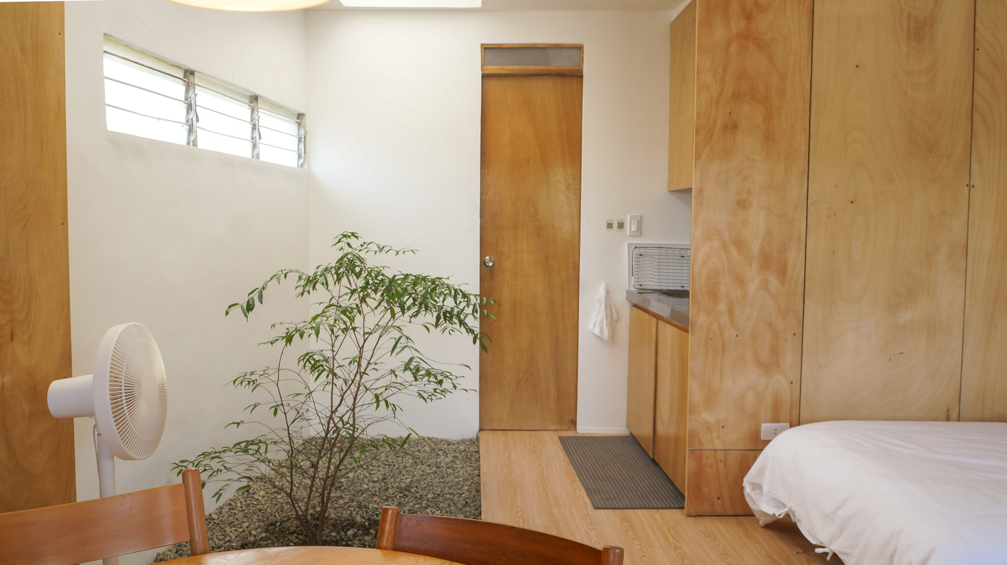 A small indoor garden with a solitary tree and gravel next to a small kitchenette.