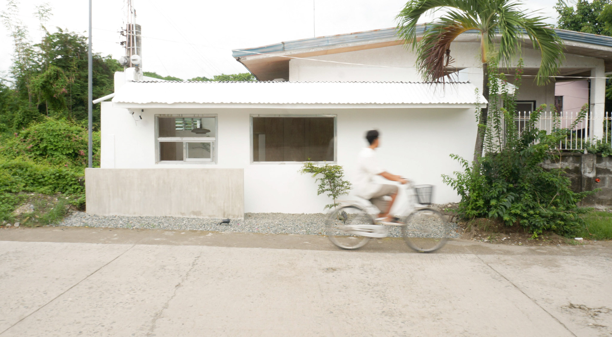 The outside of tiny house with an all white facade and person riding past in a bicycle.