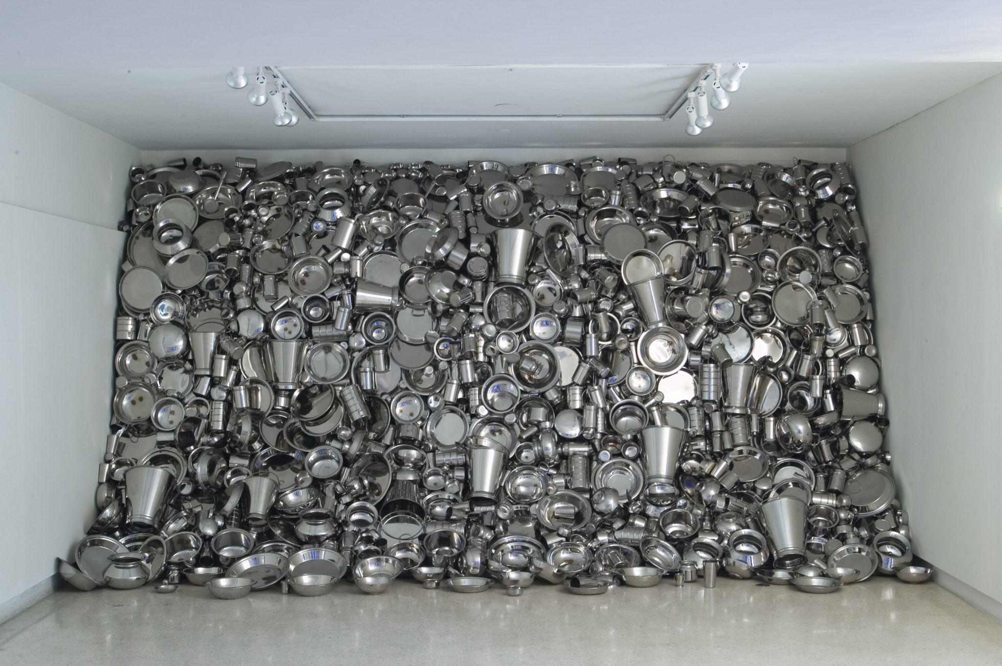 Installation art made of metal pots, pans, and containers occupying an entire wall.