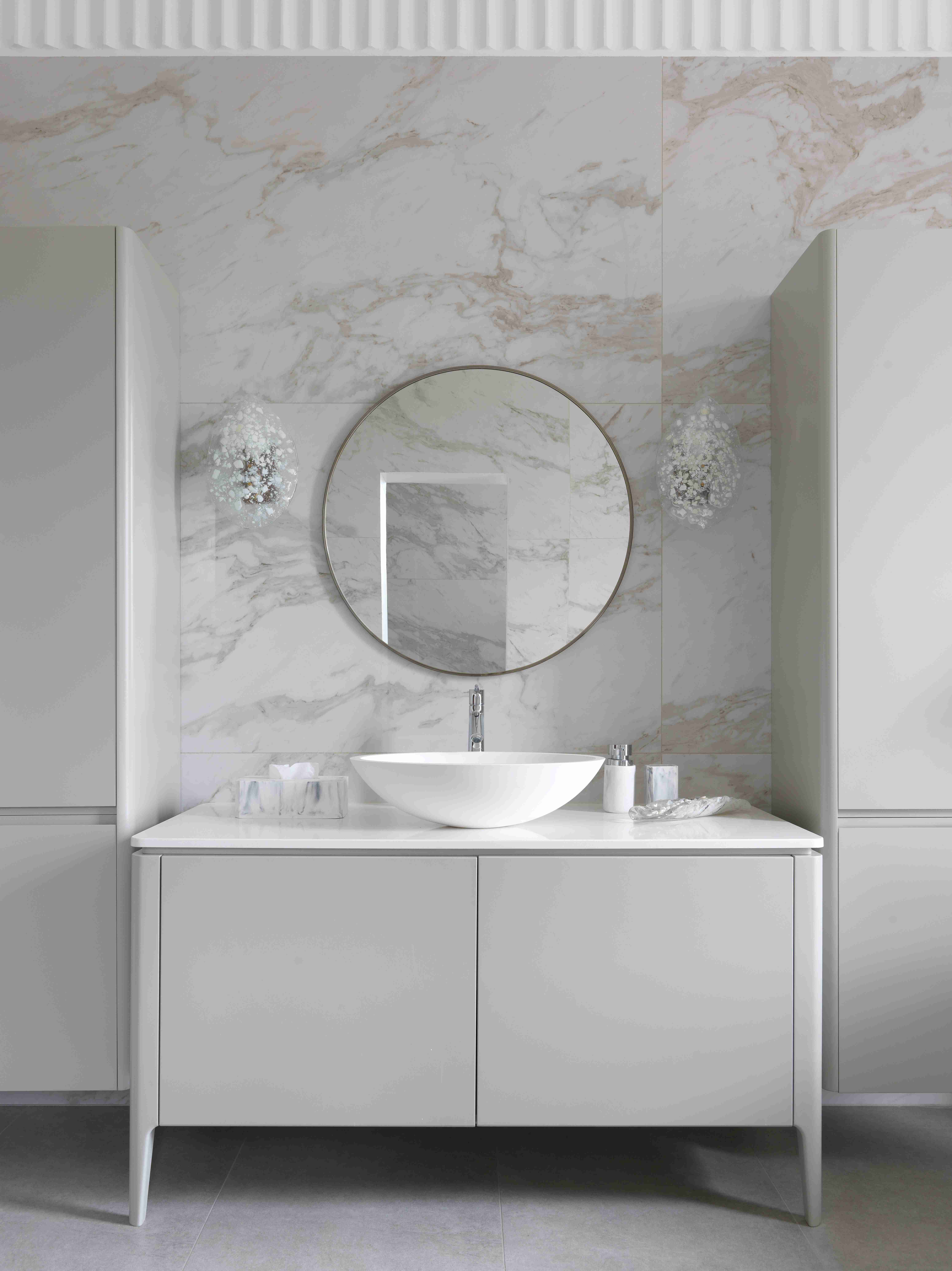 A modern white vanity with circular mirror and round basin.