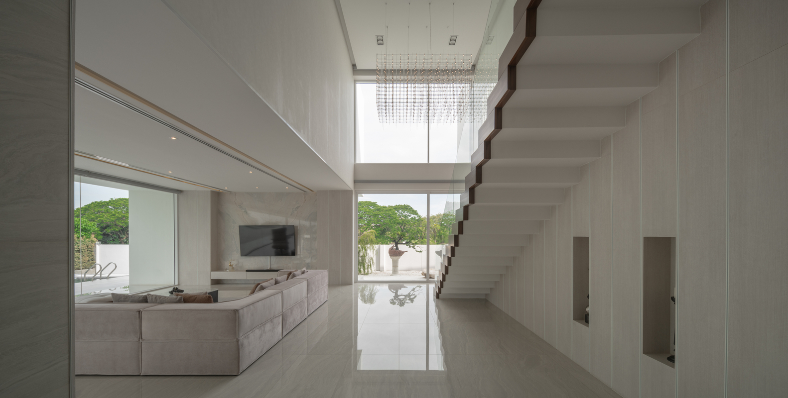 The staircase of minimalist home with double height ceilings and sectional sofa in Thailand. Photos by DOF Sky|Ground.
