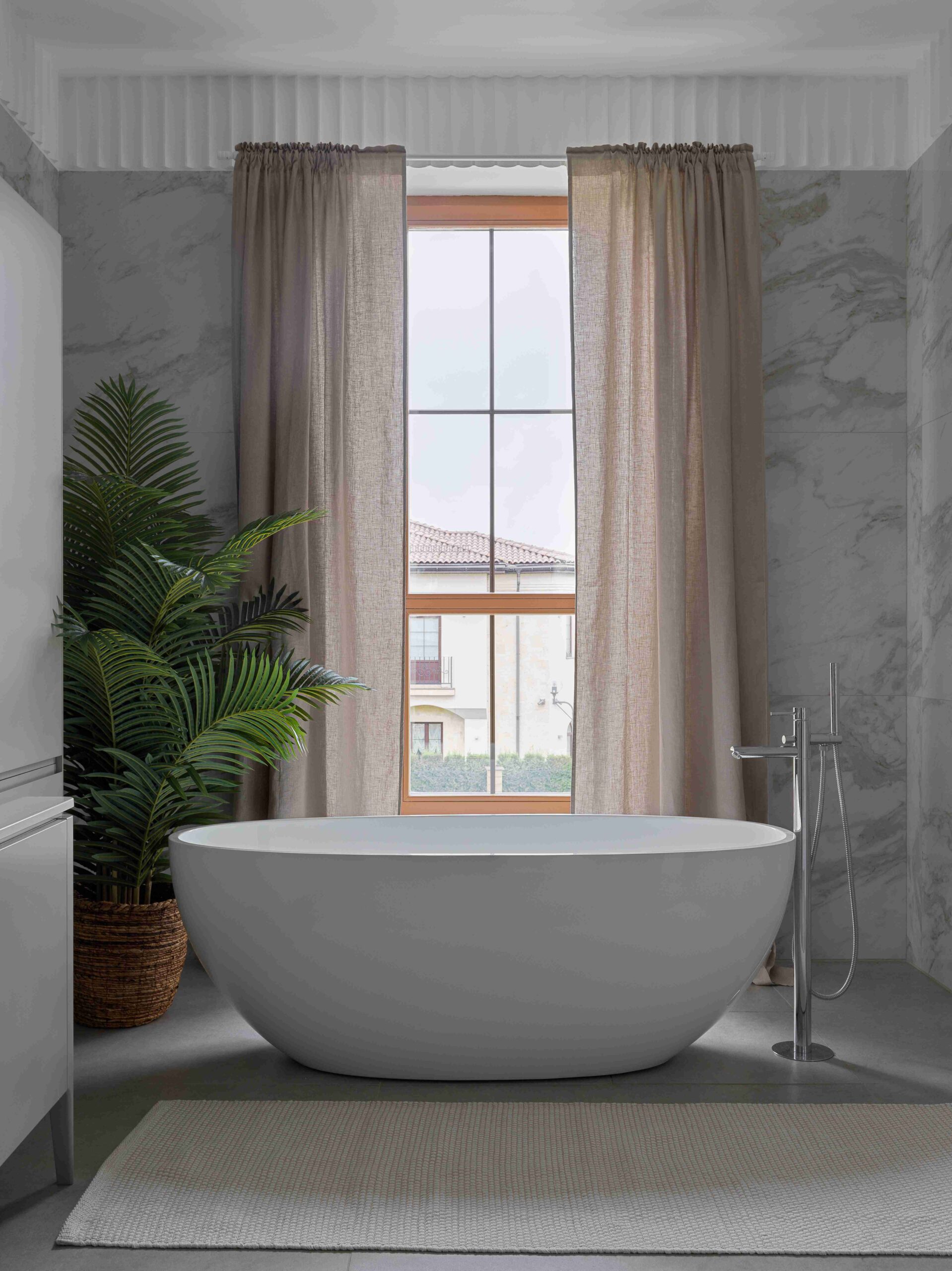 A luxurious freestanding bath tub against a floor to celiing window.