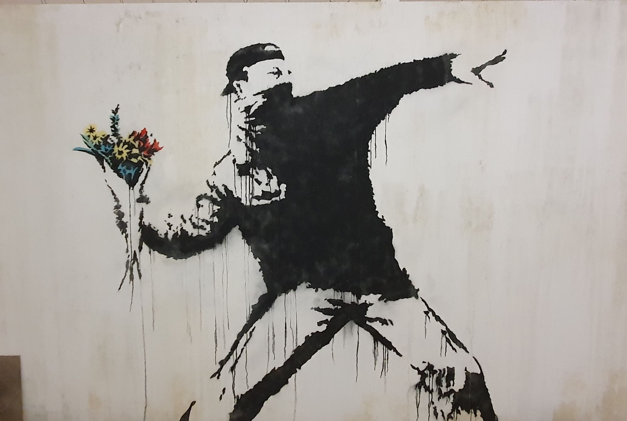 Banksy work of a masked man about to throw a bouquet of flowers.
