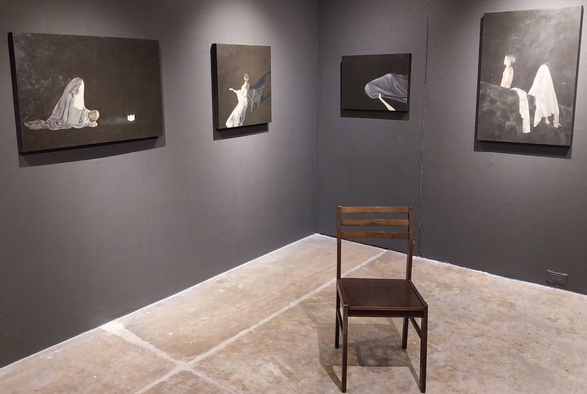 Some of the paintings for Gelo Montiero's new exhibit, with a wooden chair in the center. Photo by Elle Yap.